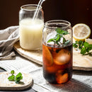 Glass of iced tea with lemon and mint leaves on a newspaper, with another glass of milk in the background.