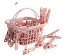 A pink plastic laundry basket filled with matching pink plastic clothes clips, with several clips scattered around on a white surface against a light blue wall.