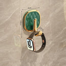 A wall-mounted hook with a faceted green glass face and gold-tone frame, shown holding a smartwatch. The image includes dimension arrows and labels indicating 6 cm width, 6.