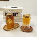 Two glass mason jars with bamboo lids and clear straws, filled with colorful drinks, displayed on oval wooden coasters in front of stacked books.