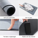 A four-panel product feature collage showing a gray rectangular mat: rolled up, being wiped with a sponge, being pinched to show flexibility, and a black phone placed on its anti-slip surface. Text labels read 'Soft and comfortable', 'Easy to clean', 'The fabric is lightweight', and 'Rubber anti-slip material'.