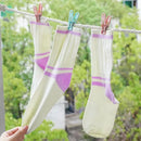 Three socks with purple stripes hanging on a clothesline against a green outdoor background.