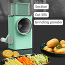 Green manual vegetable grinder with sliced vegetables and potatoes on a dark background